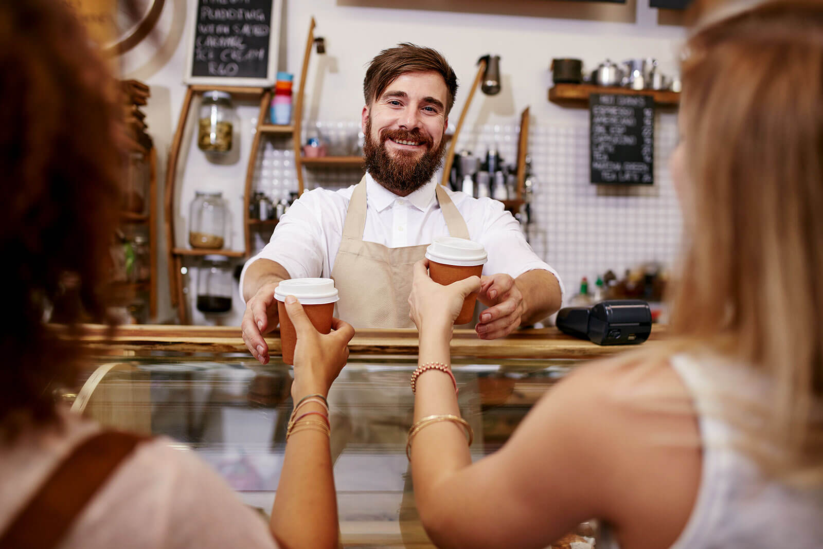 Ein Mann hinter der Theke reicht seinen Kundinnen Kaffee