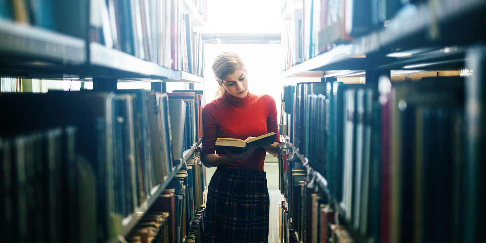 EIn Frau steht inmitten von Bücherregalen und liest