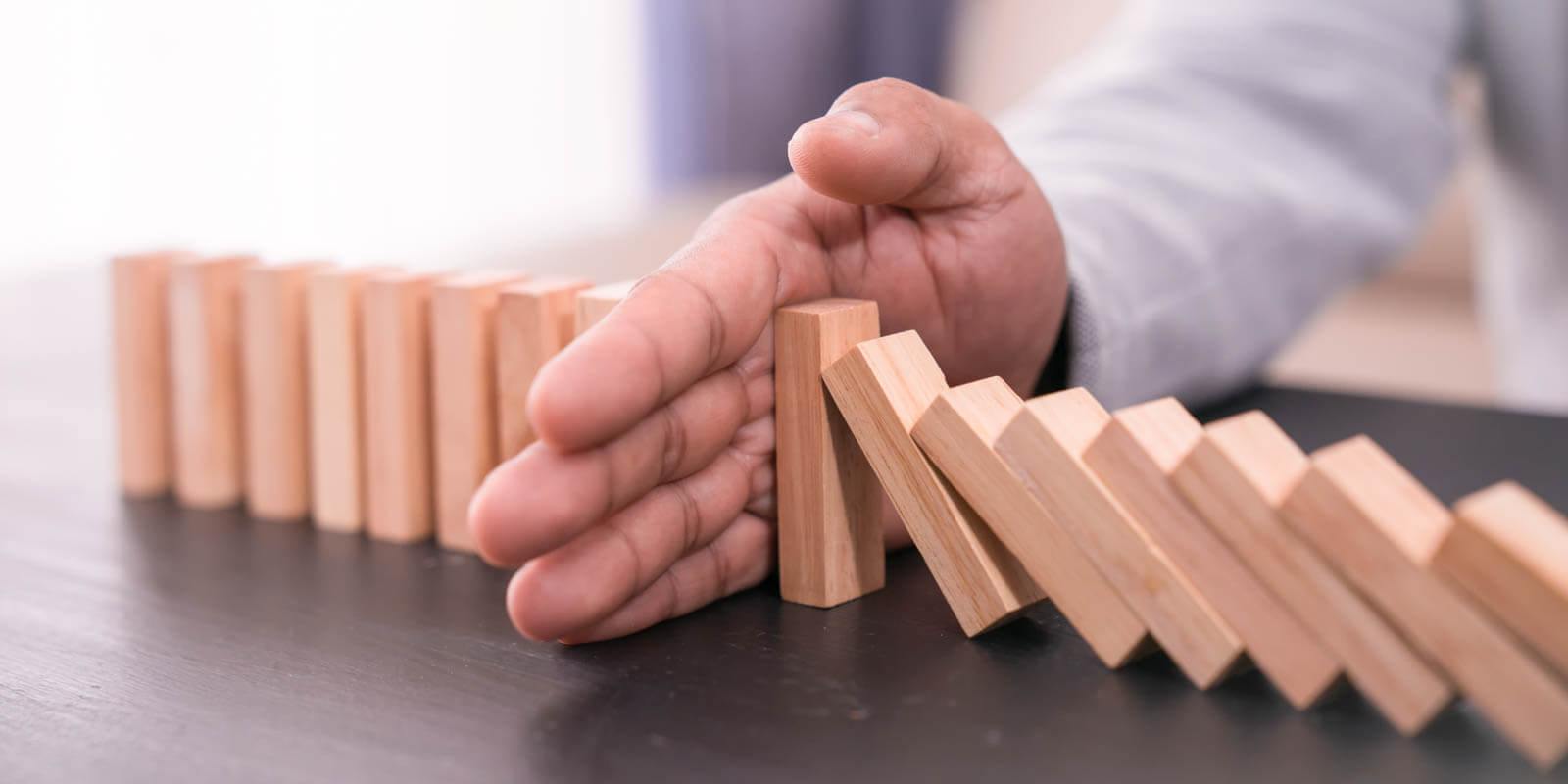 Eine Hand hält fallende Dominosteine auf